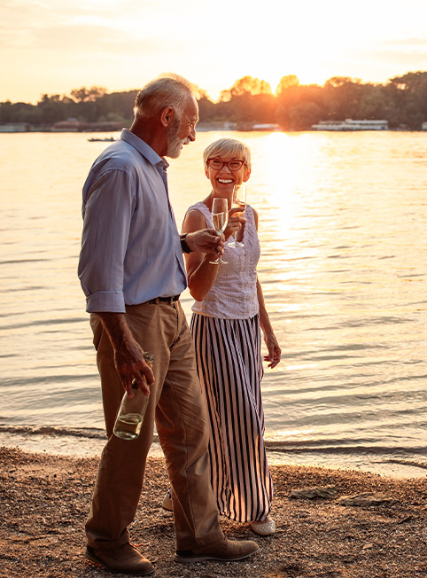 smiling couple walking on beach with glasses of wine retirement planning portsmouth nh